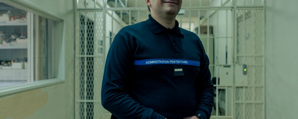 Un surveillant vêtu d'un uniforme sombre portant l'inscription « Administration pénitentiaire » se tient devant des portes grillagées dans un couloir très éclairé. Le logo Disney+ est visible dans le coin inférieur droit, laissant entrevoir cette nouvelle série.