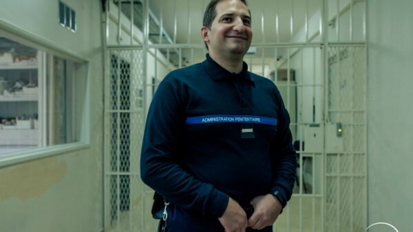 Un surveillant vêtu d'un uniforme sombre portant l'inscription « Administration pénitentiaire » se tient devant des portes grillagées dans un couloir très éclairé. Le logo Disney+ est visible dans le coin inférieur droit, laissant entrevoir cette nouvelle série.