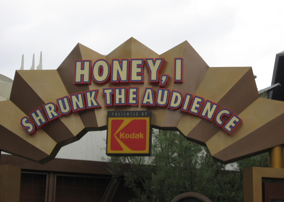 Panneau d'entrée de l'attraction « Honey, I Shrunk the Audience », présentée par Kodak, avec un lettrage stylisé et des formes géométriques. Cette attraction a remplacé « Captain EO » et est restée l'une des préférées du public jusqu'à sa fermeture, le 17 août 1998.