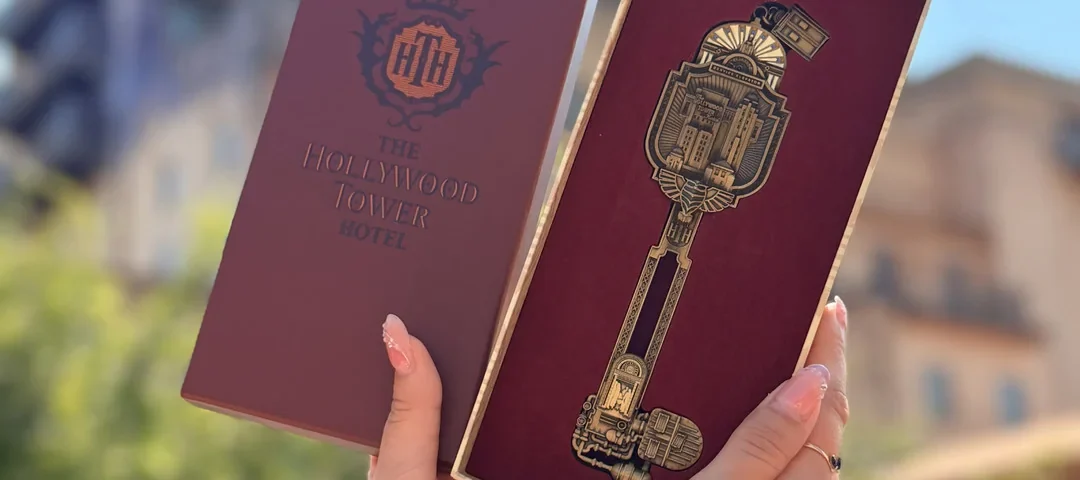 Deux mains tiennent une boîte décorative représentant l'Hollywood Tower Hotel et une clé dorée ouvragée devant un bâtiment en plein air, capturant ainsi l'atmosphère emblématique de la Twilight Zone Tower of Terror à Disneyland Paris. Cet objet de collection en édition limitée est un incontournable pour les fans à la recherche d'une touche de magie Disney et d'une élégance mystérieuse.