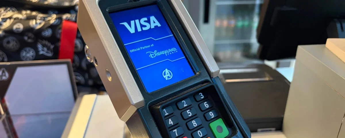 Gros plan sur un terminal de paiement par carte affichant un écran Visa avec le logo de Disneyland Paris dans un magasin, mettant en avant la technologie moderne des terminaux de paiement.