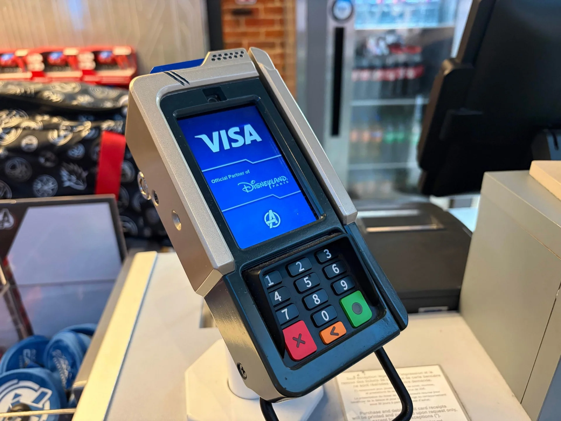 Gros plan sur un terminal de paiement par carte affichant un écran Visa avec le logo de Disneyland Paris dans un magasin, mettant en avant la technologie moderne des terminaux de paiement.