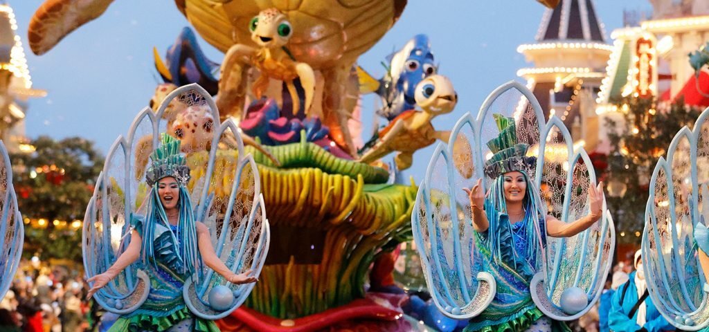 Des artistes vêtus de costumes bleus dansent devant un immense char de parade représentant des personnages du film « Le Monde de Nemo », dont une tortue de mer géante, lors de la nouvelle parade organisée à Disneyland Paris, pour le plus grand plaisir des visiteurs dans une rue du parc d'attractions en 2028.