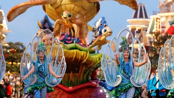 Des artistes vêtus de costumes bleus dansent devant un immense char de parade représentant des personnages du film « Le Monde de Nemo », dont une tortue de mer géante, lors de la nouvelle parade organisée à Disneyland Paris, pour le plus grand plaisir des visiteurs dans une rue du parc d'attractions en 2028.