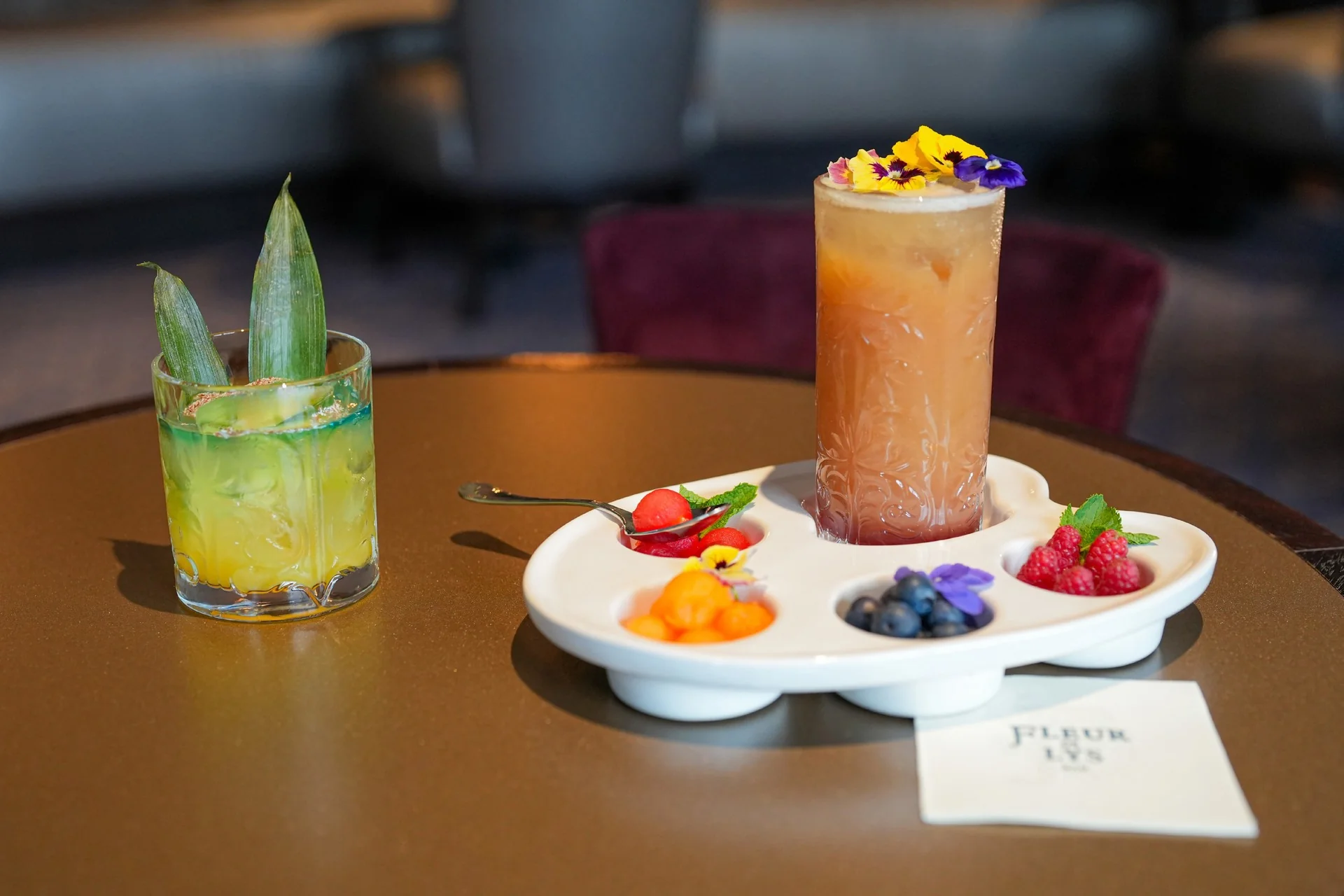 Deux cocktails trônent sur une table à Disneyland Paris ; l'un est de couleur jaune-vert et orné de feuilles, tandis que l'autre, garni de fleurs, est servi sur un plateau en forme de palette sur lequel sont disposés des baies et des fruits. Cette scène pleine de vie incarne à la perfection l'esprit festif de la Semaine internationale des princesses 2026.