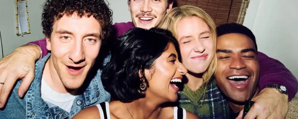 Cinq jeunes adultes sourient et rient ensemble, serrés les uns contre les autres, en posant pour une photo prise en intérieur, qui rappelle une photo de groupe tirée d’une série télévisée populaire comme la « saison 2 » de la série acclamée « Adults » diffusée sur FX.