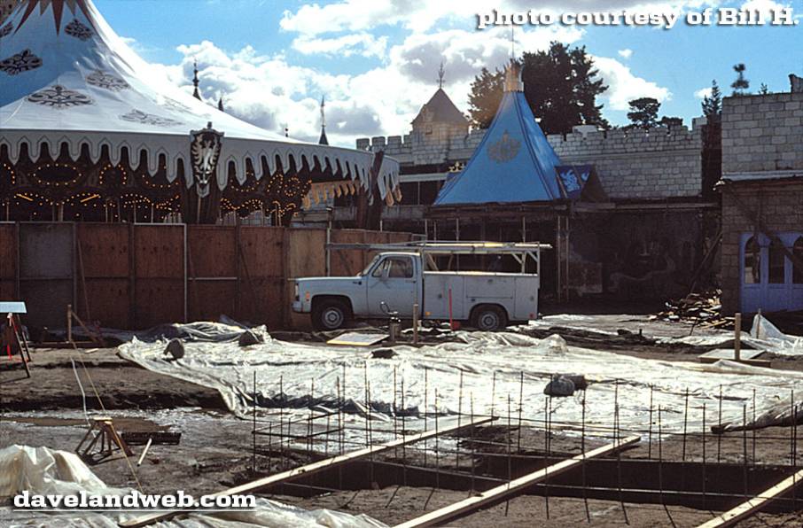 Un chantier situé dans le nouveau Fantasyland de Disneyland présente un pick-up blanc, des tentes, des bâtiments inspirés des châteaux et un sol recouvert de bâches en plastique laissant apparaître des barres d'armature, illustrant ainsi la transformation qui a débuté le 25 mai 1983.