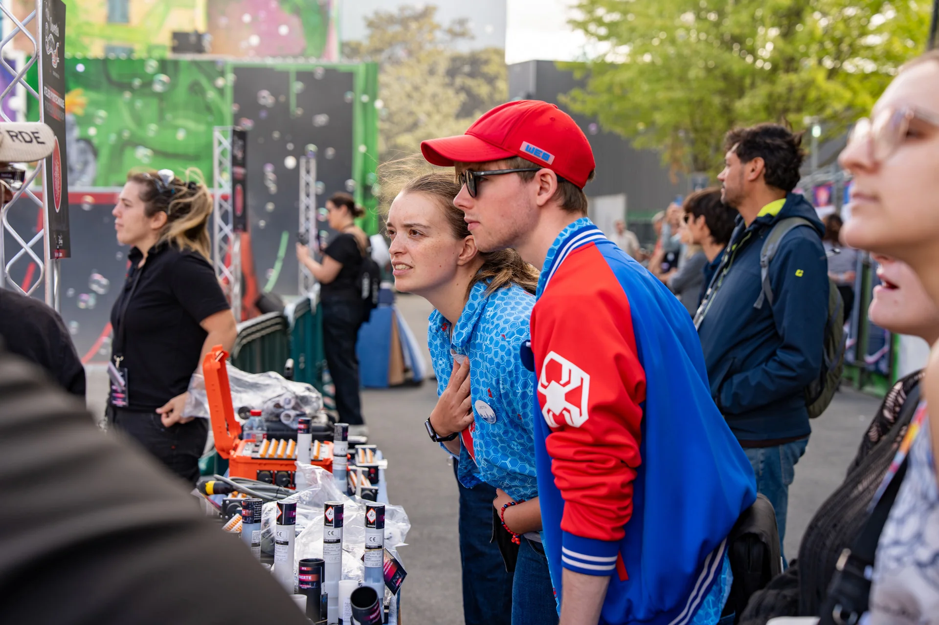 Deux personnes examinent attentivement les articles exposés sur le stand d'un vendeur lors d'un événement en plein air, entourées d'autres visiteurs et d'une multitude de produits — une ambiance qui rappelle la créativité et l'émerveillement souvent mis en scène par les équipes SFX de Disneyland Paris, où les effets spéciaux donnent vie à chaque mise en scène.