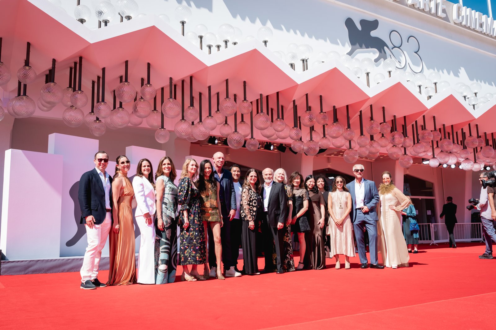Un groupe de personnes en tenue de cérémonie pose ensemble sur un tapis rouge lors d'un événement en plein air, devant une toile de fond blanche décorative, pour célébrer la première d'un documentaire de National Geographic consacré à l'Everest.