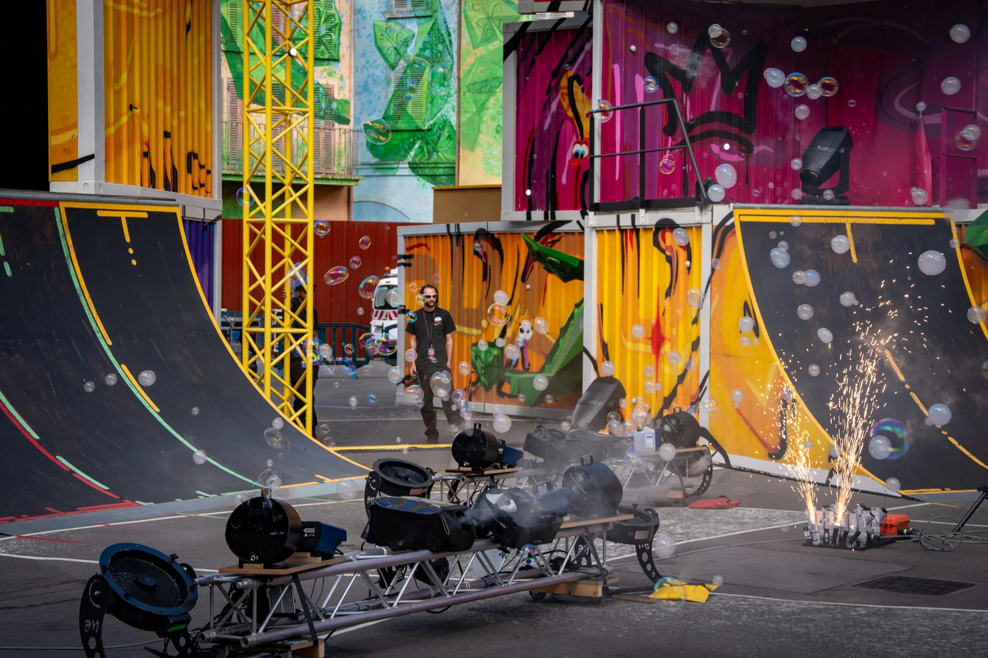 Une personne se tient entre des murs recouverts de graffitis colorés et des rampes de skate, avec au premier plan des projecteurs, de la fumée, des bulles et des feux d'artifice — offrant un aperçu de l'univers haut en couleur créé par les équipes SFX et effets spéciaux de Disneyland Paris.