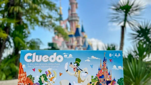 Une personne tient entre ses mains une édition exclusive du jeu de société « Cluedo » de Disney devant le château de la Belle au bois dormant à Disneyland Paris.