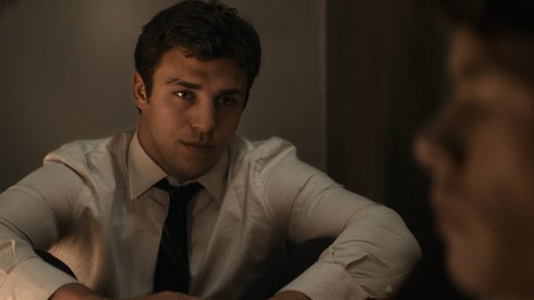 Un homme vêtu d'une chemise blanche et d'une cravate est assis et regarde une personne floue au premier plan de cette série dramatique consacrée à la NFL.