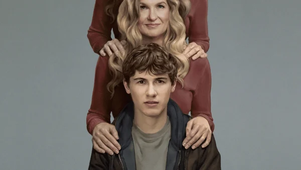 Dans cette scène de la série « Phony », une femme blonde se tient derrière un jeune homme, les mains posées sur ses épaules.