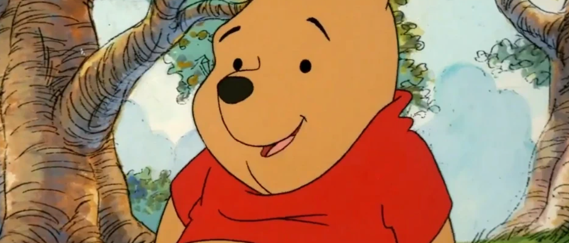 Winnie l’Ourson, vêtu d’une chemise rouge, se tient debout dans une forêt.