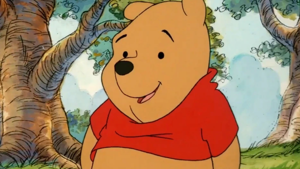Winnie l’Ourson, vêtu d’une chemise rouge, se tient debout dans une forêt.