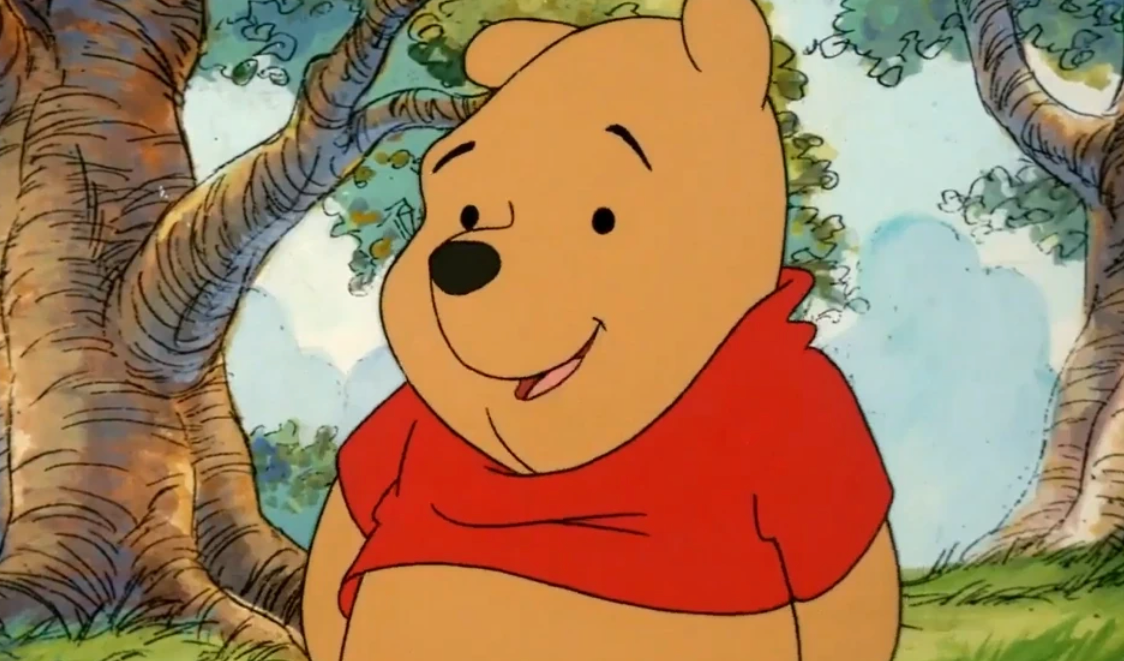 Winnie l’Ourson, vêtu d’une chemise rouge, se tient debout dans une forêt.