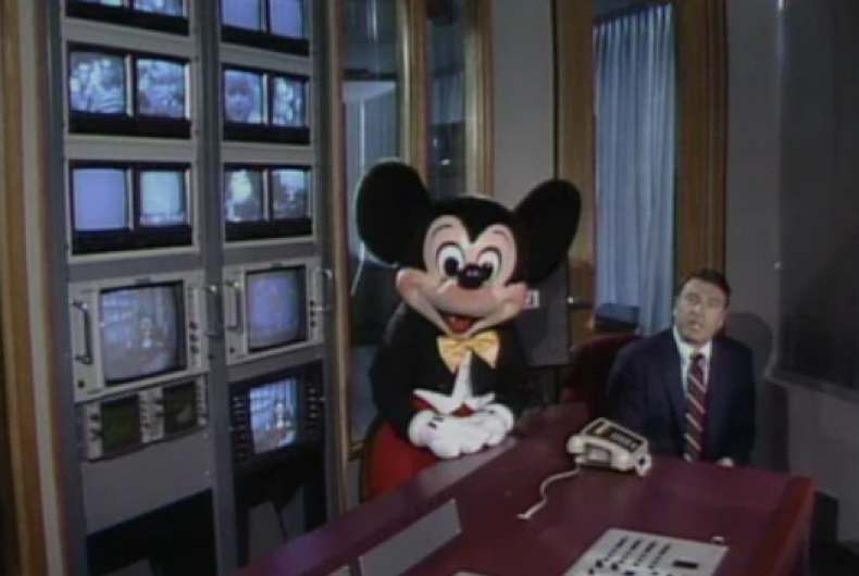 Dans une salle de contrôle, une personne vêtue d'un costume de Mickey Mouse est assise à côté d'un homme en costume, rappelant les débuts de Disney Channel, qui a été lancé le 18 avril 1983.