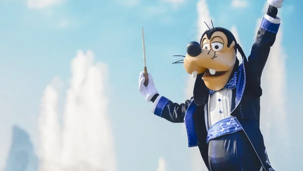 Goofy, déguisé en chef d'orchestre des Dingos, tient une baguette, le bras levé, devant une fontaine.